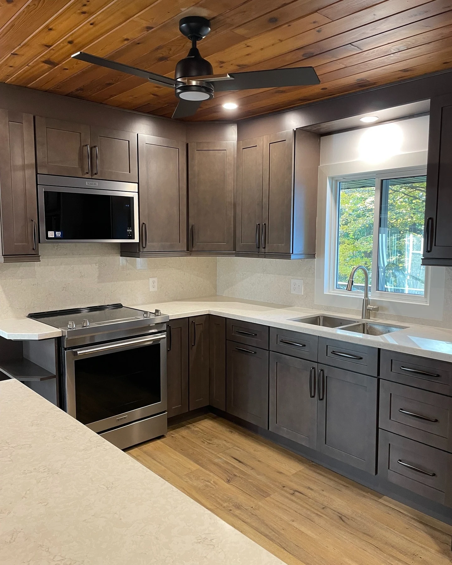 Compact kitchen with dark cabinets, white backsplash and window