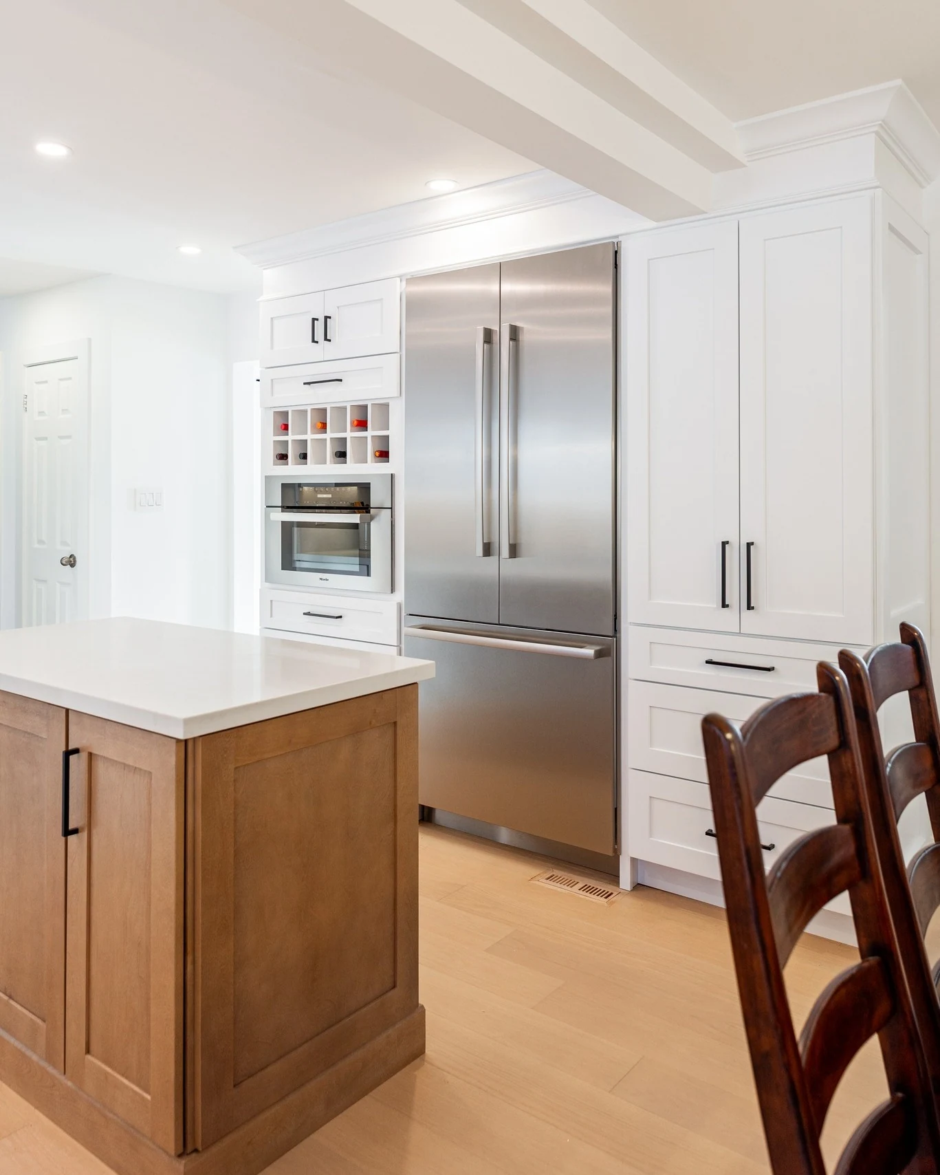 Kitchen with white wall cabinets and tall natural wood pantry storage